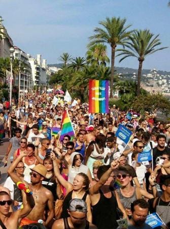 Une foule de personnes participant à une parade rose, marchant dans une rue tenant fièrement des drapeaux arc-en-ciel.