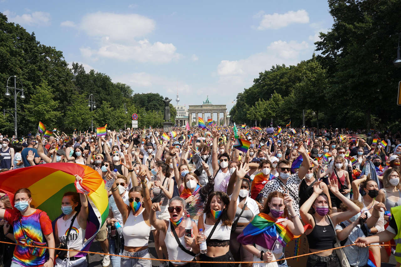 Une foule de personnes agitant des drapeaux arc-en-ciel lors de la fierté de Berlin devant la porte de Brandebourg.