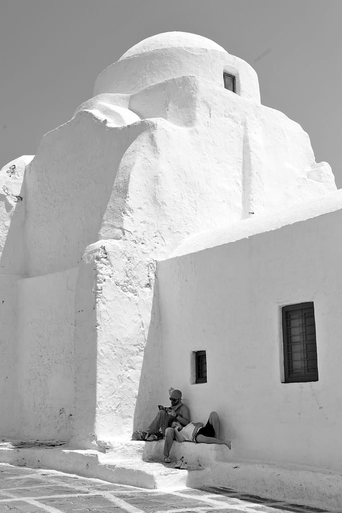 Un homme est assis sur un banc devant un bâtiment blanc à Mykonos.