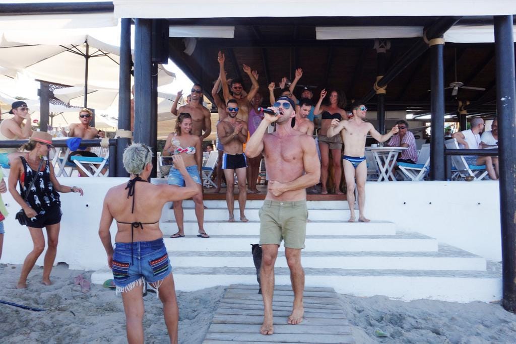 Un groupe de personnes debout sur une plage devant un bar.